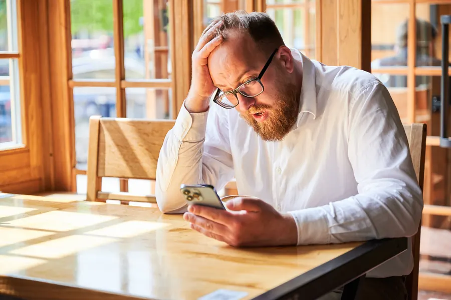 Un gérant de café, la main sur le front, lit un message sur son téléphone
