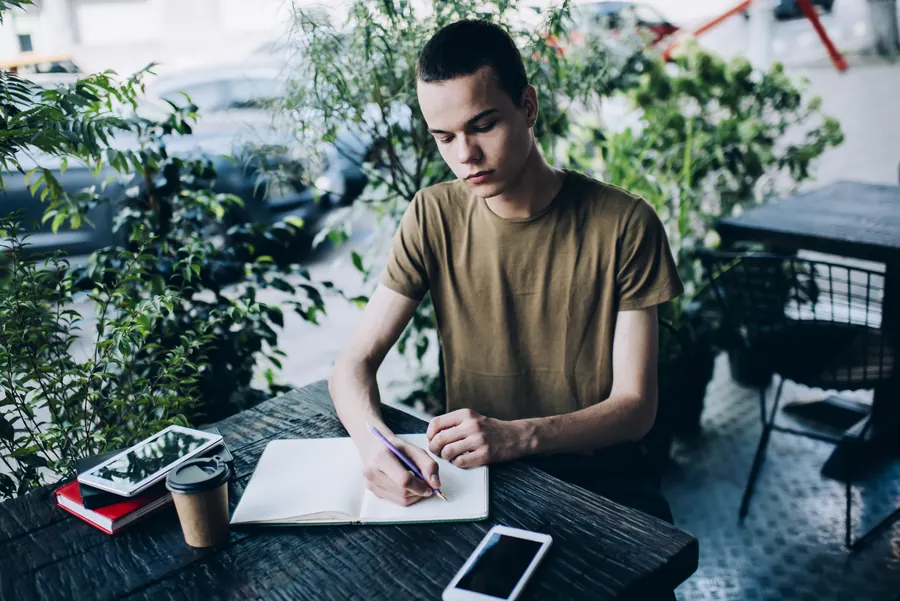 Jeune homme prenant des notes dans un carnet à une table de café