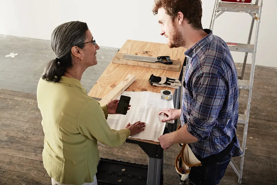 Un artisan échange avec sa cliente autour de l’établi, en fin de chantier : c’est le meilleur moment pour laisser sa carte et demander une recommandation.