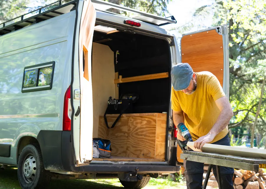Un artisan au travail à côté de sa camionnette : siglé et lisible de loin, le véhicule fait savoir à toute la rue qui travaille là.