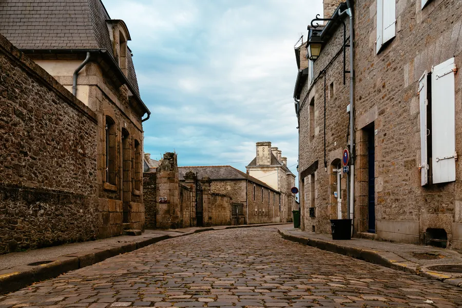 Une rue pavée déserte, bordée de maisons en granit aux volets blancs