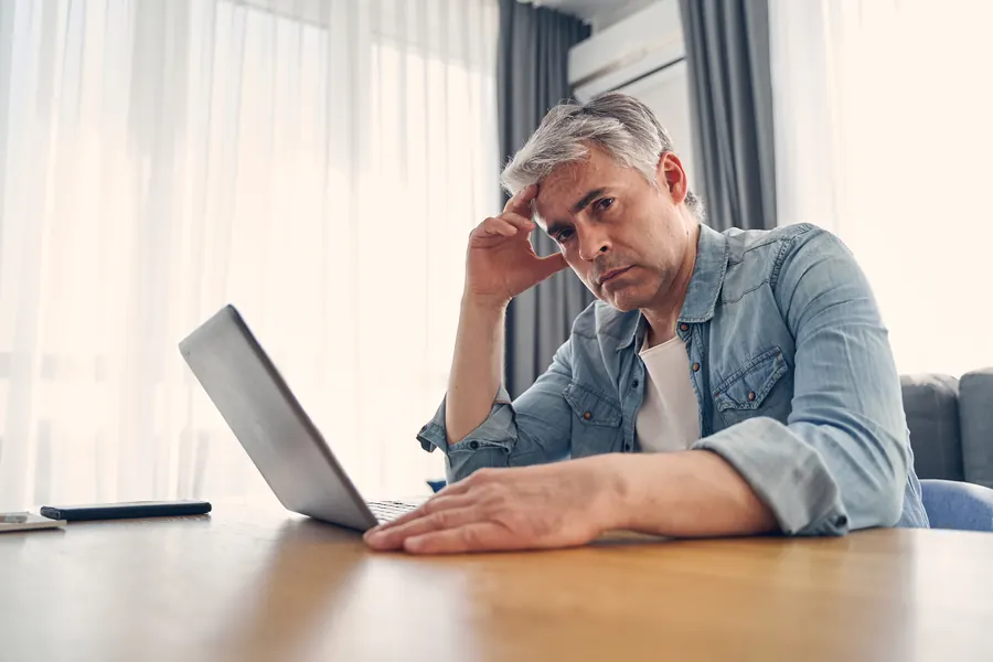 Un homme aux cheveux gris, la main sur le front, devant son ordinateur portable