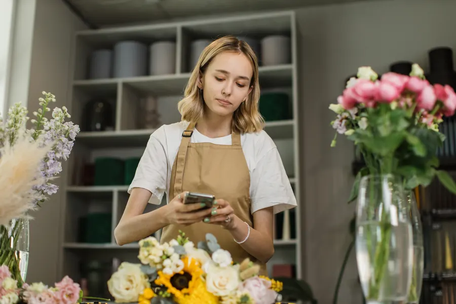 Une fleuriste met sa fiche à jour depuis son téléphone, entre deux bouquets : un quart d’heure par mois suffit à la garder exacte.