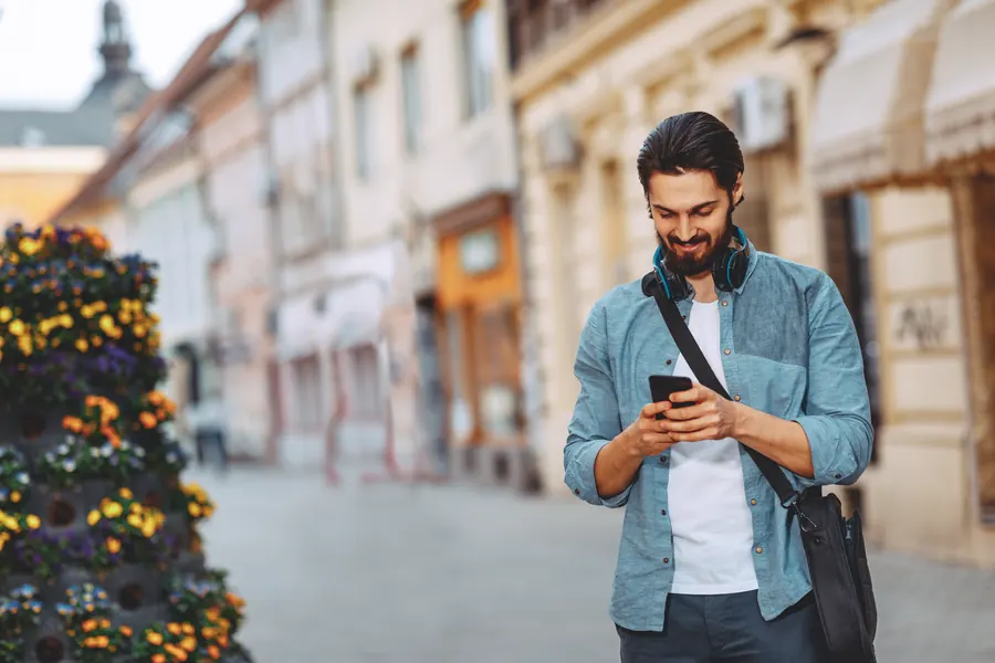 Un homme sourit en consultant son téléphone dans une rue piétonne commerçante