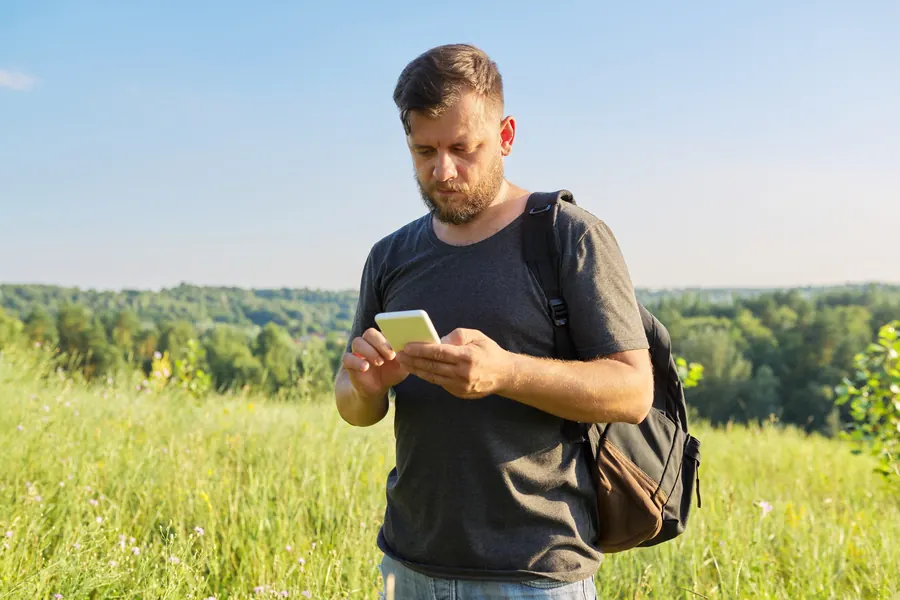 Un randonneur consulte son téléphone en pleine campagne : c’est avec ce réseau-là, pas avec la fibre du bureau, que votre site doit rester rapide.