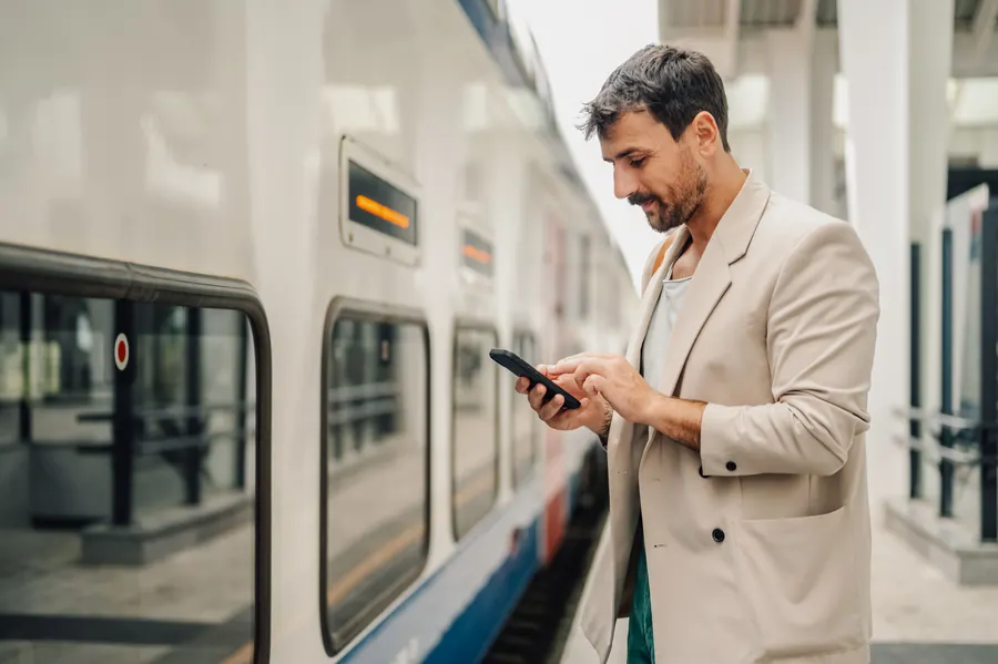 Un voyageur consulte son téléphone sur un quai de gare : les données de terrain mesurent la vitesse vécue par des visiteurs comme lui, pas celle du bureau.