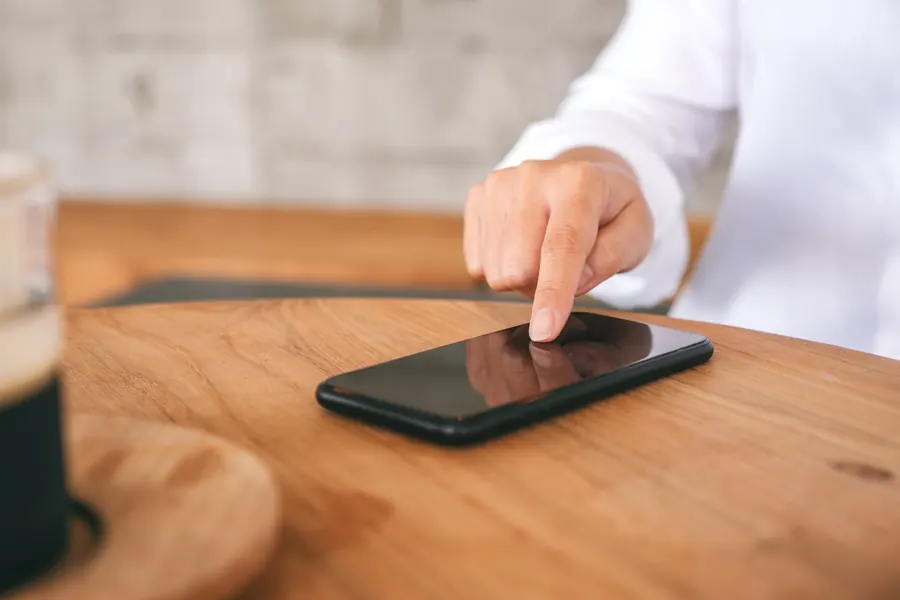 Un doigt fait défiler l'écran d'un téléphone posé sur une table en bois