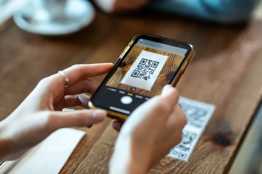 Une main scanne avec son téléphone le QR code d’une carte : la page qui s’ouvre à cet instant décide si votre numéro sera enregistré ou oublié.