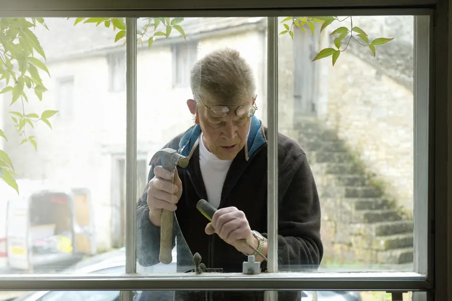 Un artisan reprend une fenêtre au marteau et au ciseau : quand la maison est saine, on répare ce qui coince sans tout reconstruire.