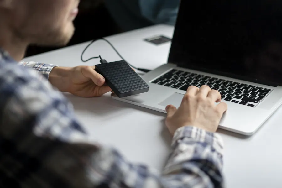 Un homme tient un disque dur externe branché à son ordinateur portable