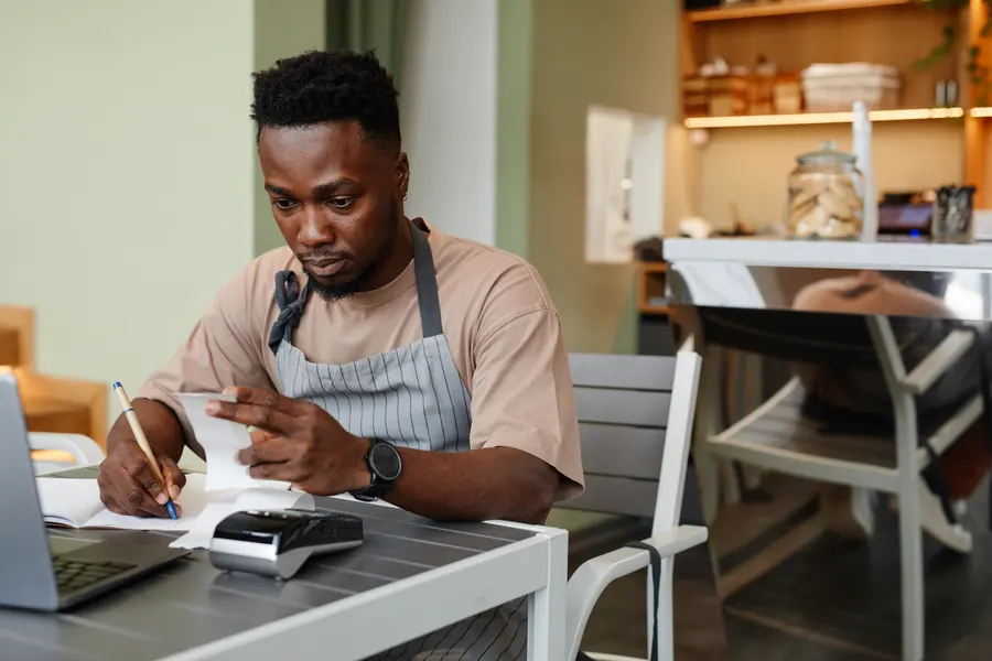 Le gérant d'un café vérifie ses tickets et ses factures, calculatrice à portée de main