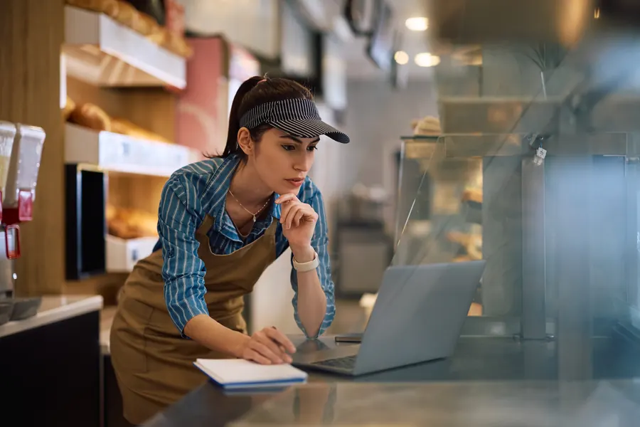 Une boulangère penchée sur son comptoir regarde son ordinateur portable d'un air perplexe
