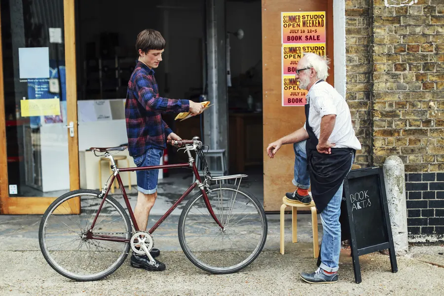 Un bouquiniste sert un client sur le pas de sa porte : la notoriété locale se construit d’abord dans la rue, puis se lit en ligne, dans les avis et les mentions.