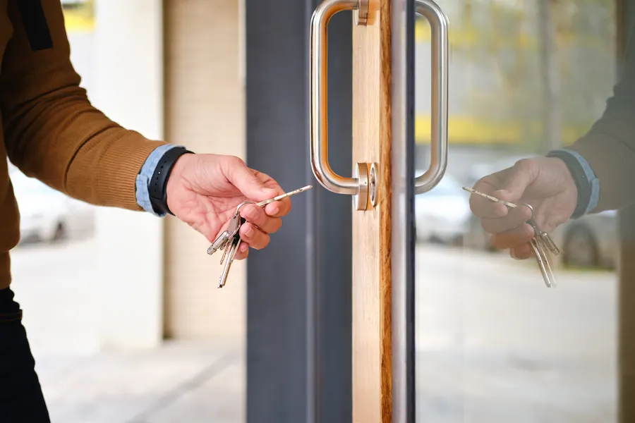 Une main tourne la clé d’une porte vitrée : garder son nom de domaine à son nom, c’est garder la clé de sa présence en ligne.