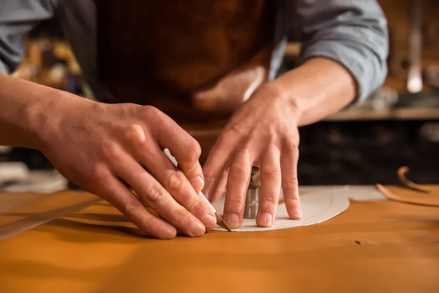 Artisan découpant une pièce de cuir au cutter, sur son établi
