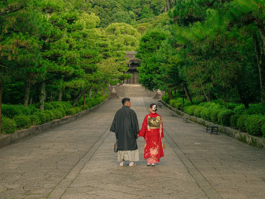 Couple en tenue traditionnelle de dos sur une allée bordée d'arbres verts