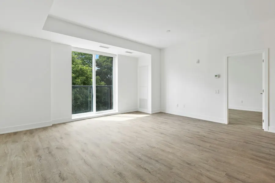 Séjour vide et lumineux avec parquet et porte-fenêtre sur un balcon verdoyant