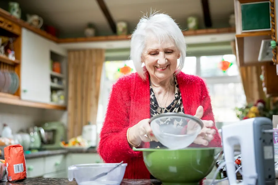 Dame âgée souriante qui prépare un saladier dans une cuisine chaleureuse