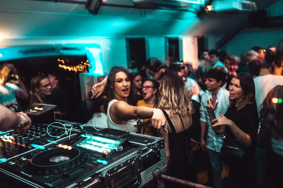 Console de DJ au premier plan devant une foule qui danse sous des lumières bleues