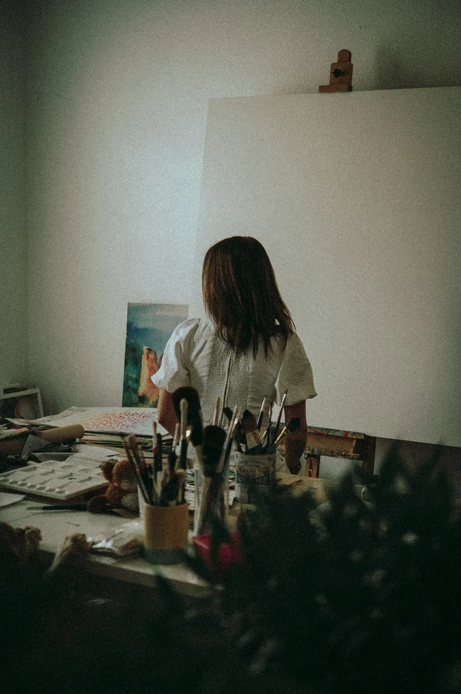 Peintre de dos dans un atelier clair, pinceaux et toile de paysage
