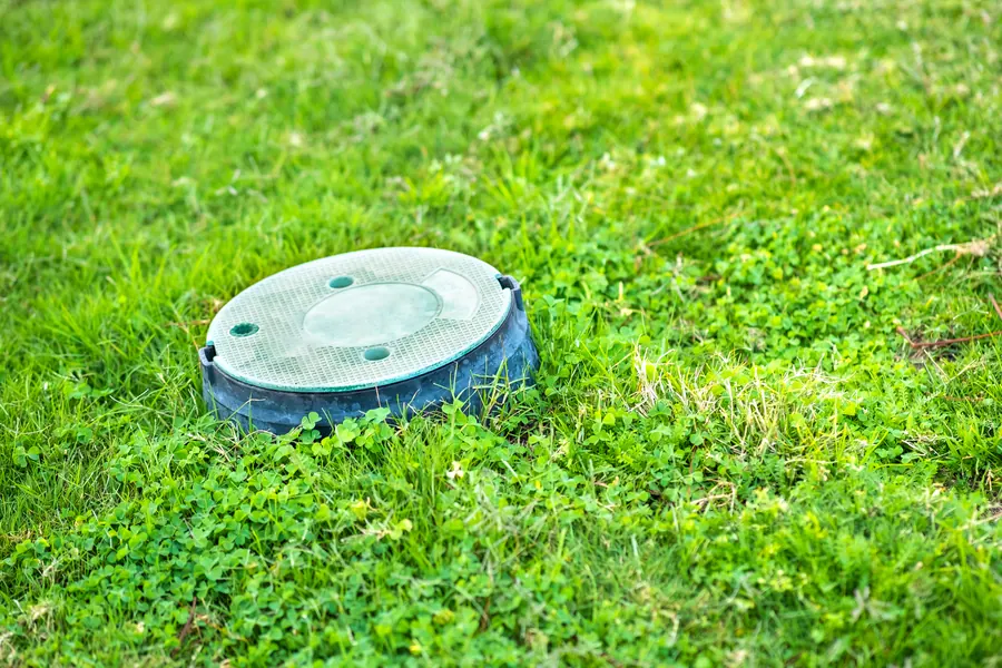 Maison de campagne en pierre, pelouse nette, deux tampons verts de regards dans l'herbe