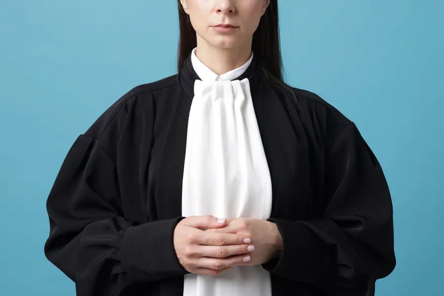 Robe noire d'avocat avec rabat blanc suspendue à un portemanteau, dossiers à côté