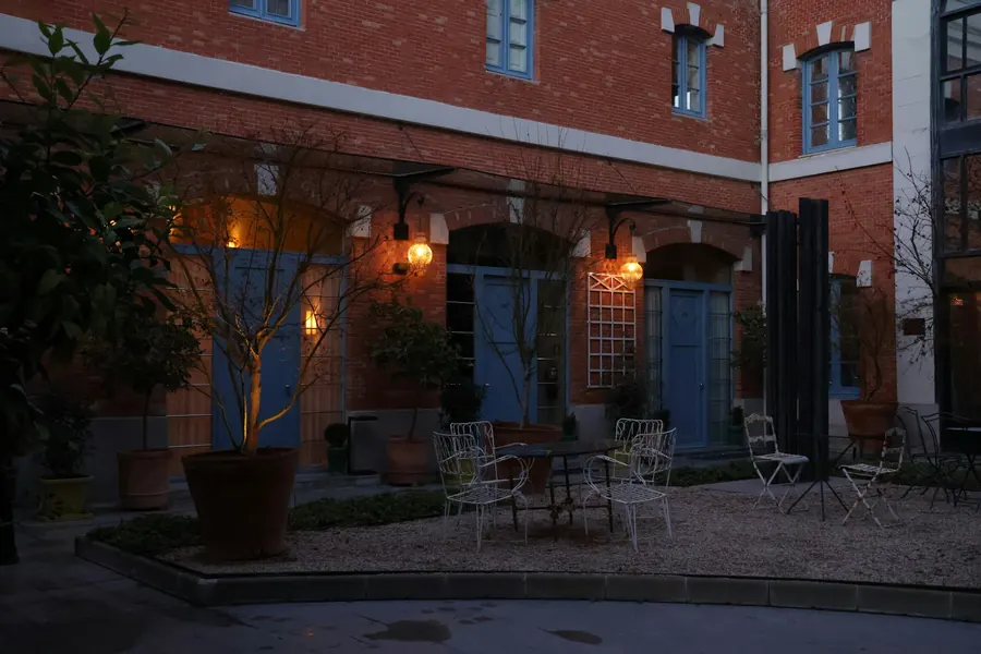 Cour pavée d'un ancien atelier, guirlandes lumineuses, tables en bois, à la tombée du jour