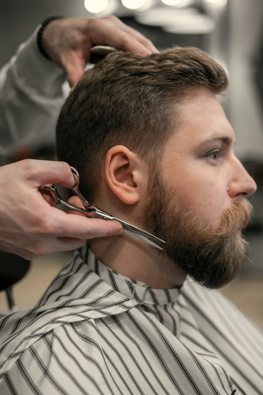 Barbier qui taille une barbe au peigne et aux ciseaux, lumière de vitrine