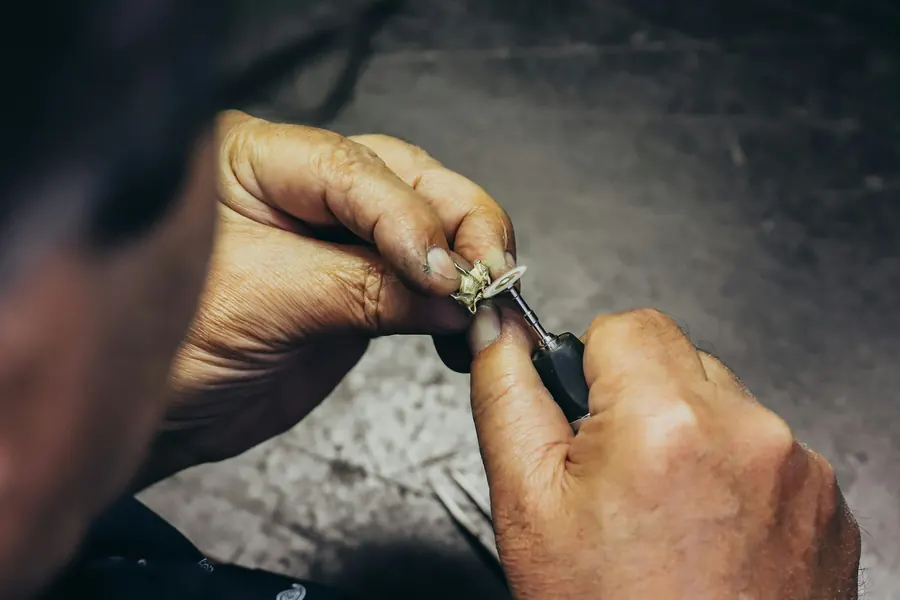 Mains d'un bijoutier qui sertit une pierre sur une bague à l'établi