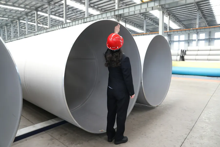 Femme casquée qui inspecte de grands tubes d'acier dans un hall d'usine lumineux