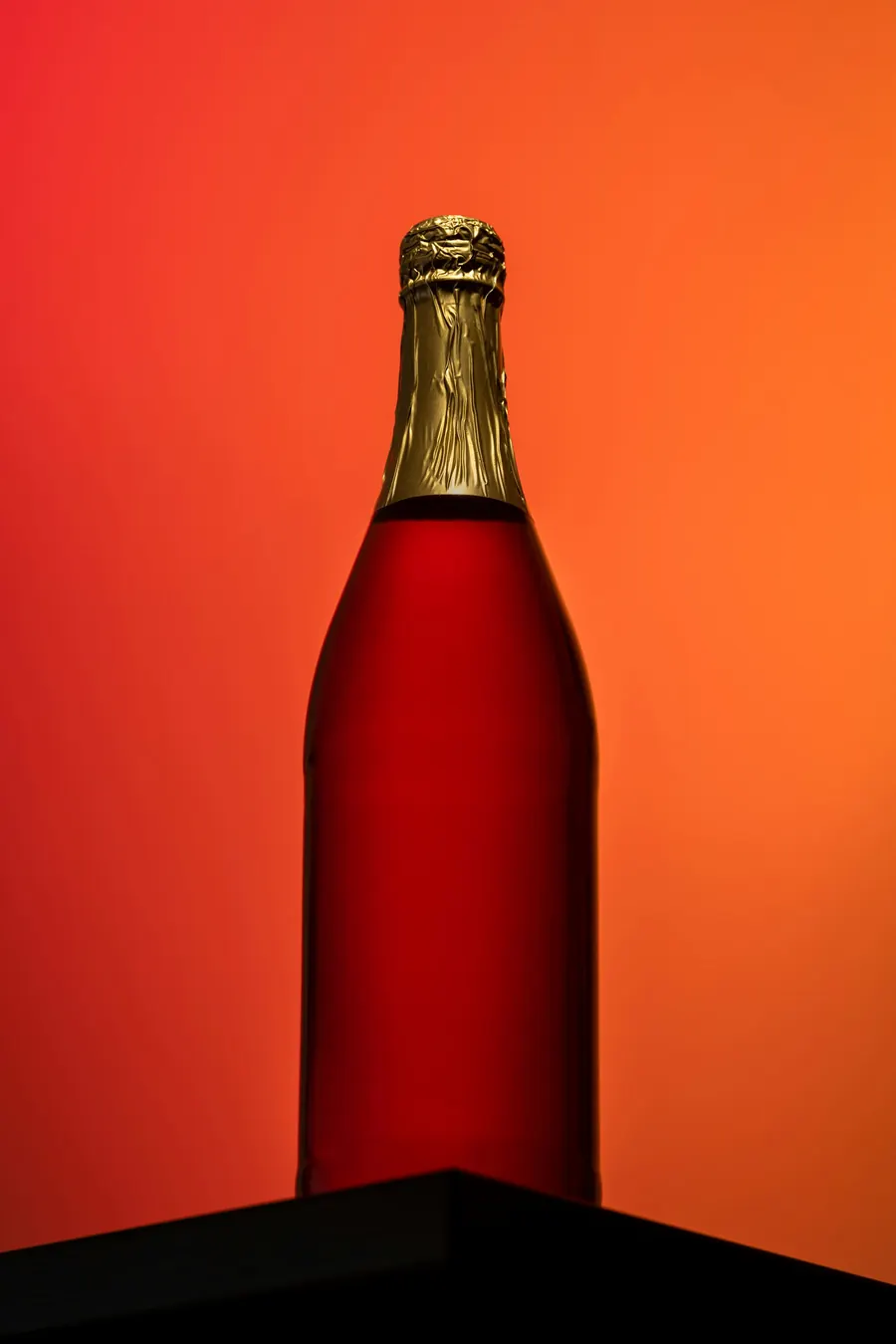 Bouteille de style champagne au liquide rouge, fond orange, sans étiquette