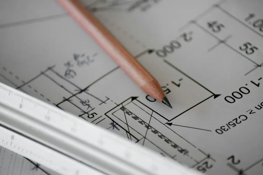 Plans de structure annotés au crayon, règle et calculatrice sur un bureau