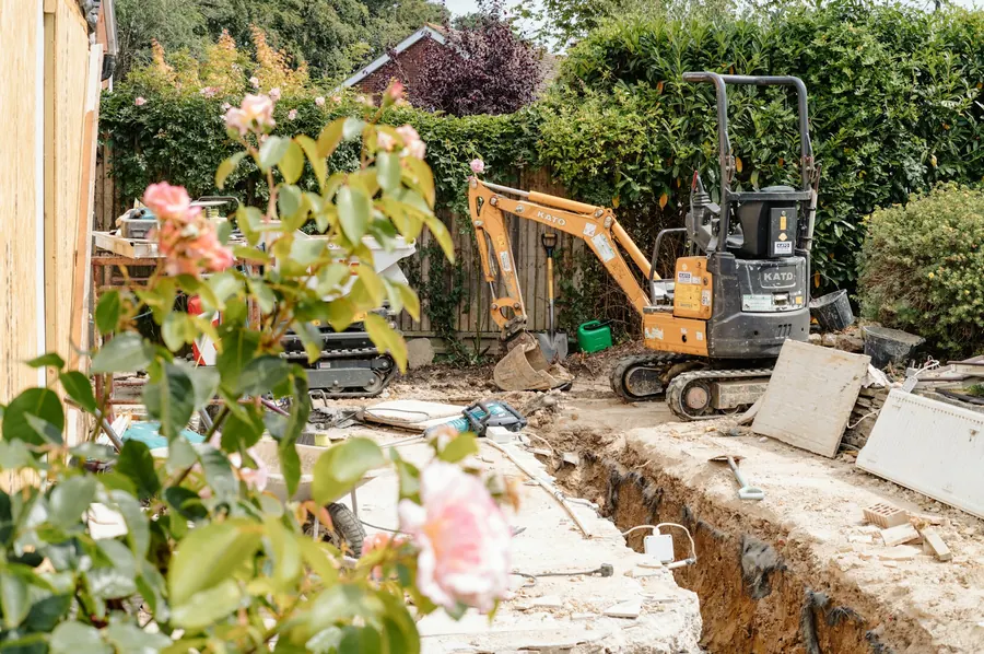Mini-pelle qui creuse une tranchée contre la façade d'une maison