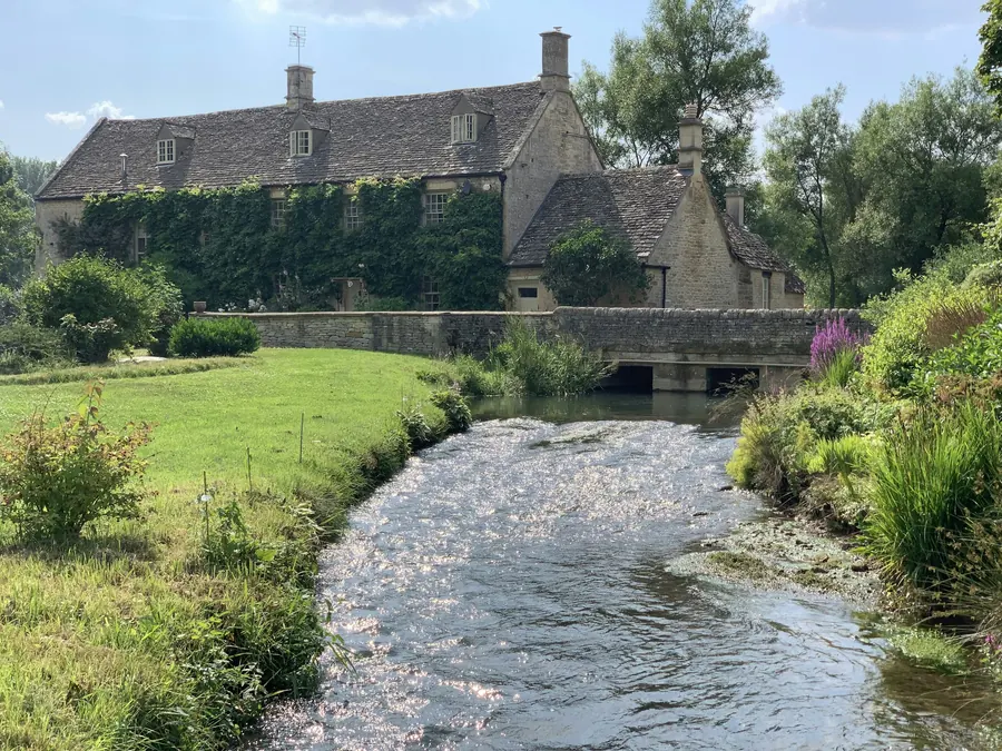 Grande bâtisse en pierre couverte de lierre au bord d'une petite rivière