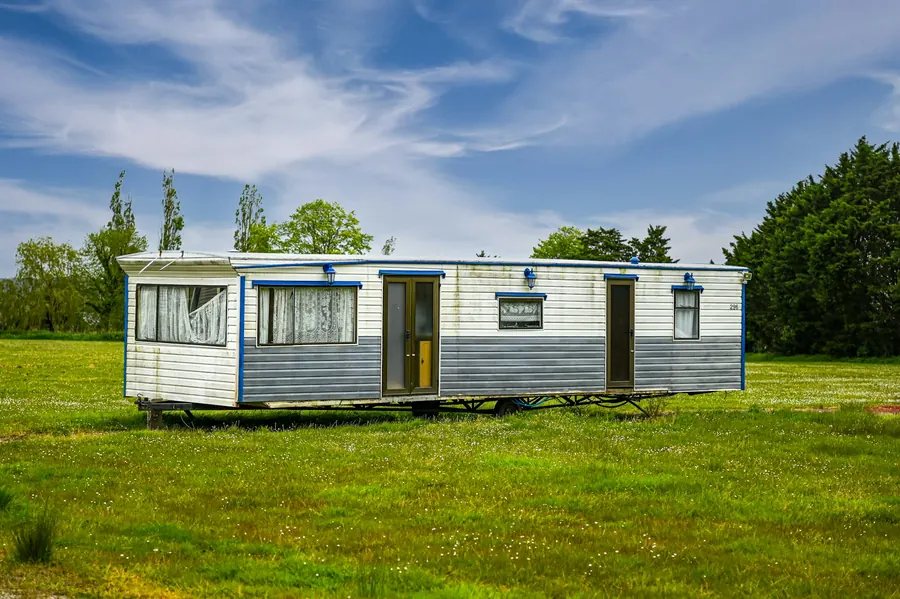 Mobil-home isolé dans un grand champ herbeux sous un ciel bleu