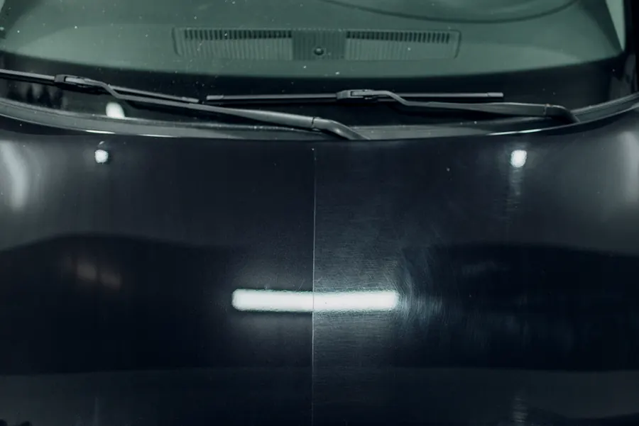 Capot repeint brillant, reflets des néons de l'atelier
