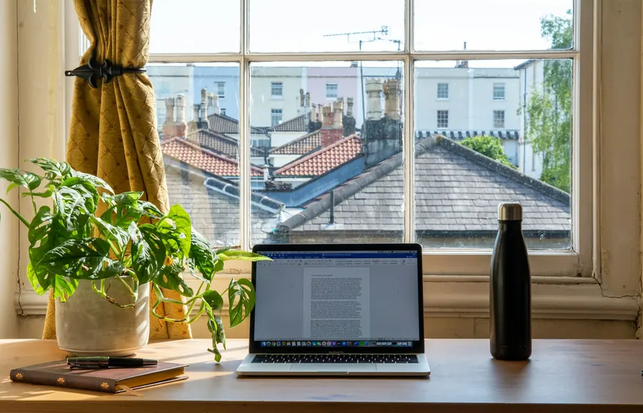 Petit bureau fermé, poste installé avec ordinateur portable, fenêtre sur cour, plante verte