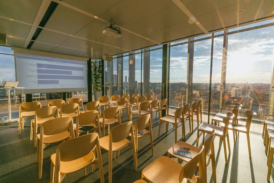 Grande salle vitrée avec rangées de chaises sous une verrière métallique