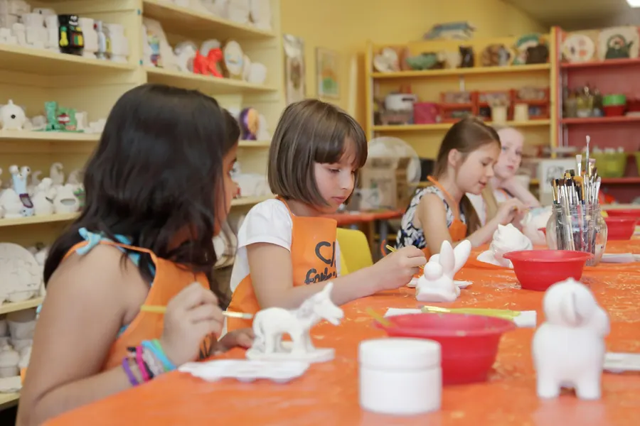 Groupe de fillettes qui peignent des figurines à une table d'atelier