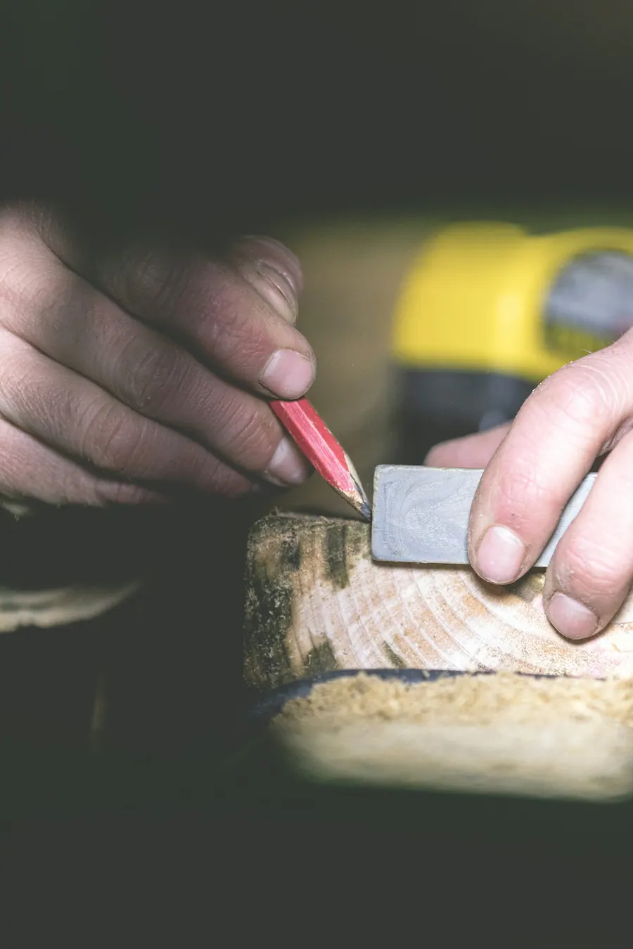 Charpentier qui trace une pièce de bois à l'équerre et au crayon, sciure sur l'établi