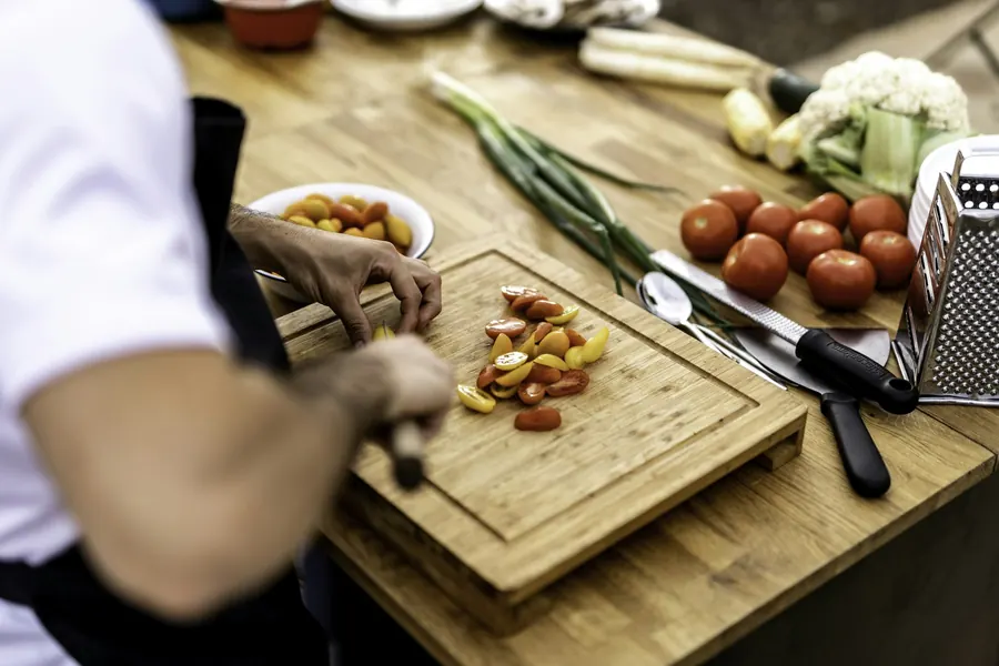 Mise en place sur un plan de travail d'appartement : planche, couteaux, légumes taillés, mains du chef