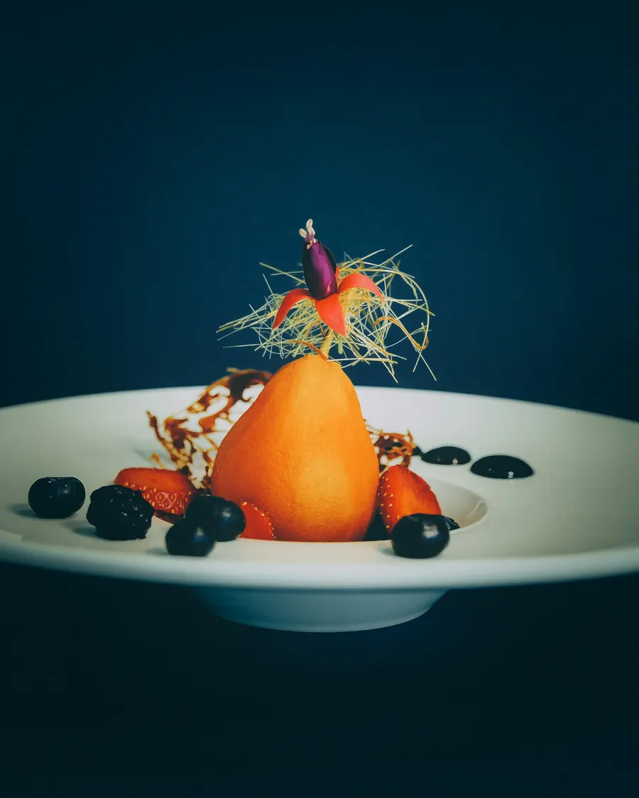 Poire pochée entière dressée avec fruits rouges sur assiette blanche
