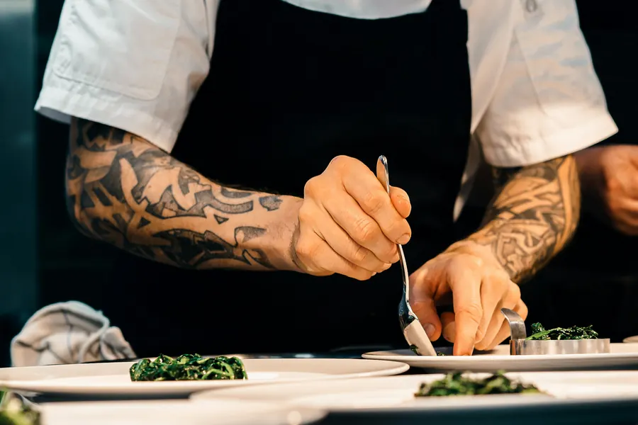 Mains d'un chef en tablier qui dresse des assiettes à la pince