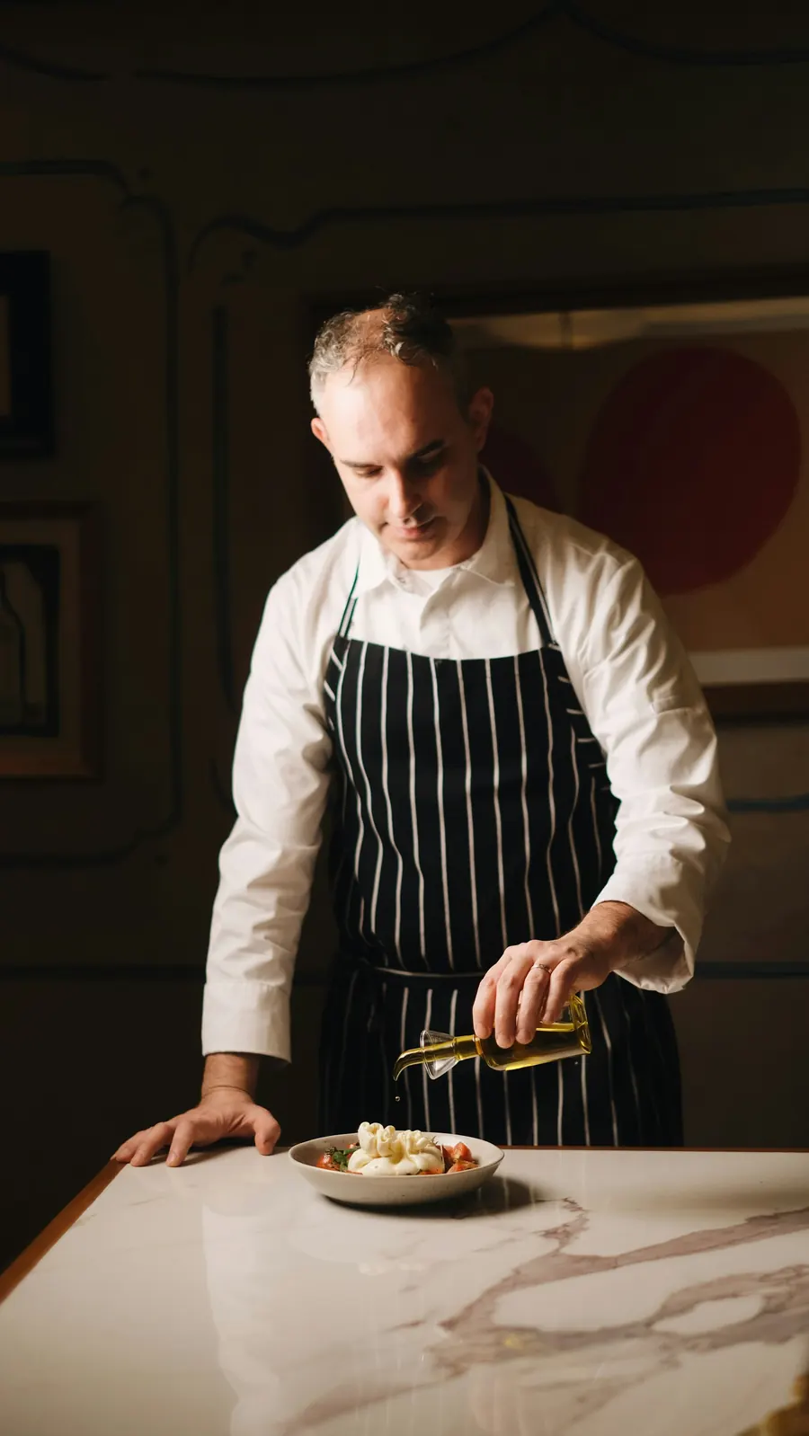 Chef en tablier rayé sombre dans une cuisine claire, mains actives