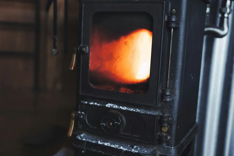 Poêle à bois noir avec grande vitre et flamme, gros plan dans un intérieur rustique