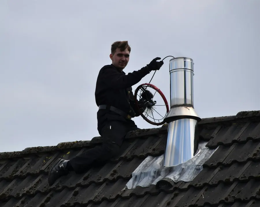 Ramoneur sur le toit qui nettoie un conduit métallique