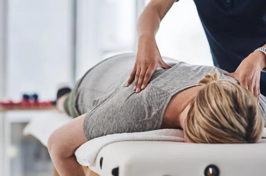 Les mains de la praticienne posées sur le haut du dos d'un patient allongé, lumière du jour, pas de blouse
