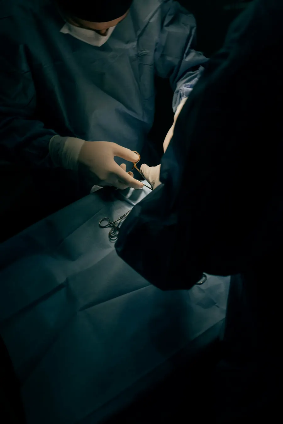 Mains gantées d'un chirurgien qui suture, gros plan, champ opératoire flou