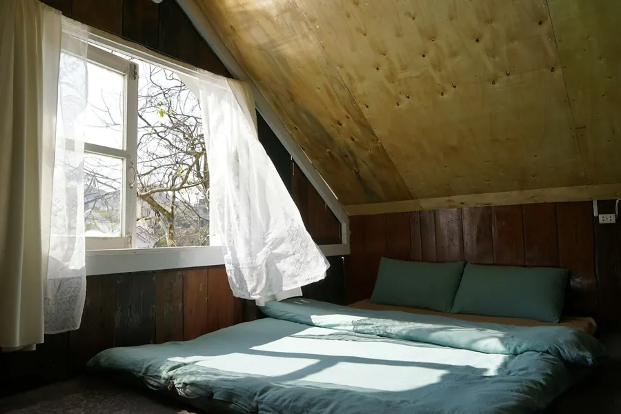 Chambre mansardée aux poutres apparentes, lumière d'été, sans climatiseur visible