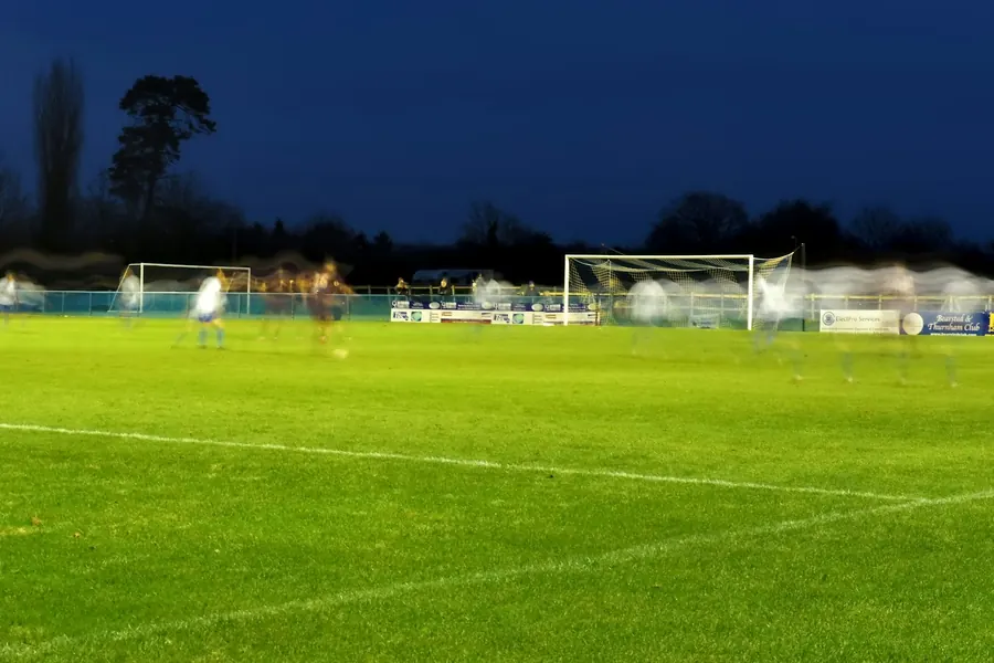 Terrain de football éclairé au crépuscule, bâtiments en arrière-plan